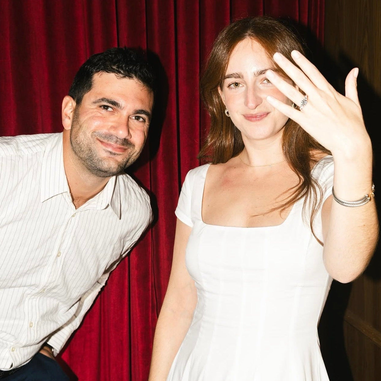 Man and woman posing together in front of a red curtain